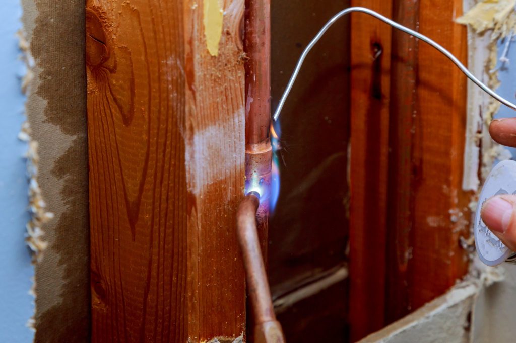 Closeup professional master plumber hands soldering copper pipes gas burner pipe line repair